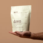 Hand holding a package of 'dawn' broth against a brown background